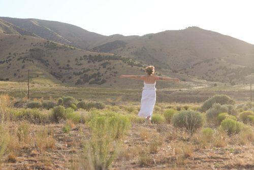 girl with white dress on running in a field with arms wide open, feeling free and unbounded.