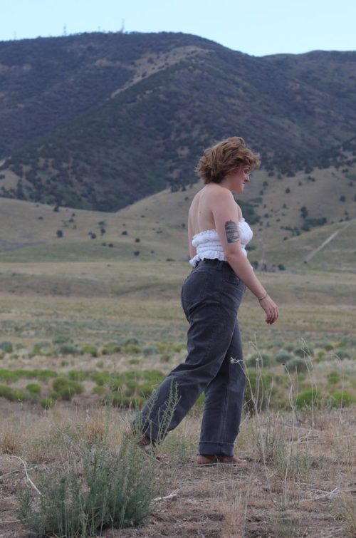 girl walking through a field with mountains in the background