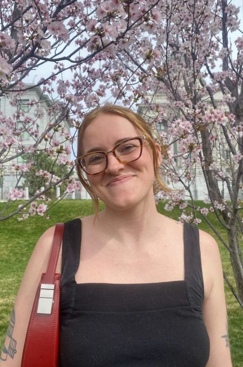 girl with red hair and glasses posing in front of a cherry blossom tree